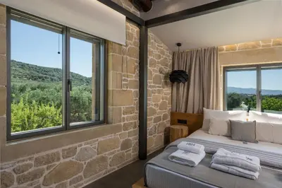 a bedroom with a stone wall and a bed with windows at Semes luxury villas in Drapaniás