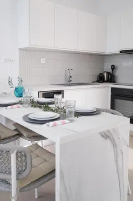 a white kitchen with a table with plates and glasses at Niki Luxury Suites Pool Resort 200m From Beach in Chorafakia
