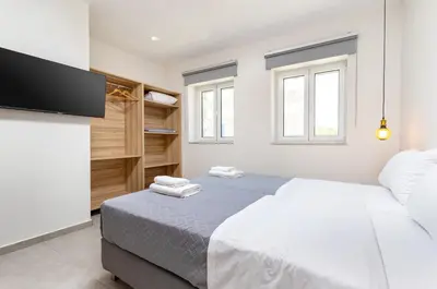 a white bedroom with two beds and a flat screen tv at Meli apartments Paleochora in Palaiochóra