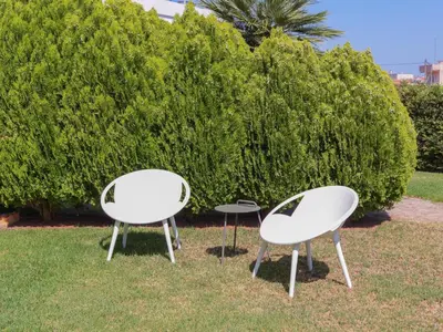 two white chairs in the grass near a bush at Cisterna Apartment - Shared Pool in Stérnai