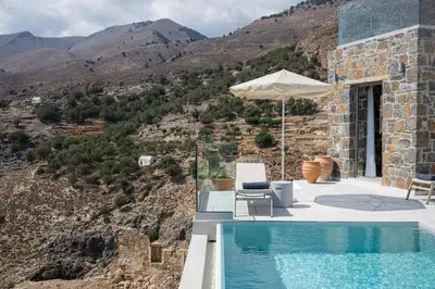 a pool with chairs and an umbrella next to a mountain at Villa Dóma in Sfakiá