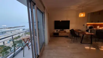 a room with a balcony with a television and a table at Sea View Modern 2BR Top Floor on Nea Chora Beach in Chania Town