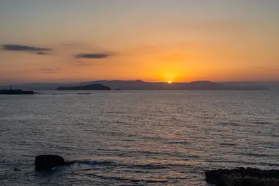 a sunset over a body of water with mountains in the background at Waves - Seaside Escape in Chania Town