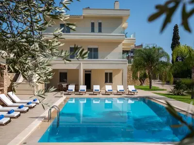 a pool in front of a building with chairs and a house at Villa Melitini in Souda