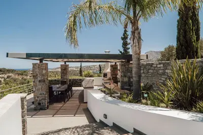a patio with a table and chairs and palm trees at Villa Kera Panorama by PosarelliVillas in Vamos