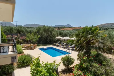 a pool in a yard with chairs and a palm tree at Villa Aetheria by PosarelliVillas in Plátanos
