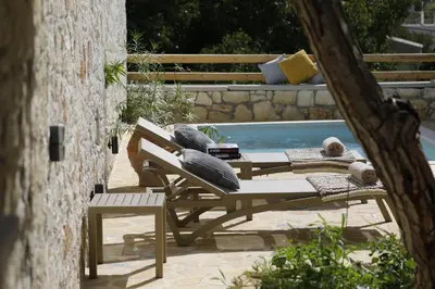 a bench and a table with pillows next to a pool at Tholos by Praxithea Stone House & Pool in Gavalochori