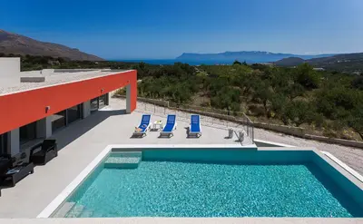 a swimming pool on the side of a building with blue chairs at Gramvousa Villas in Kissamos