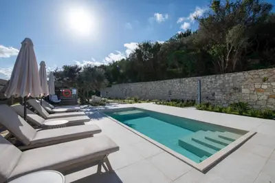 a swimming pool with lounge chairs and an umbrella at Villa Mareli - Beachside Villa with Heated Pool in Almirida