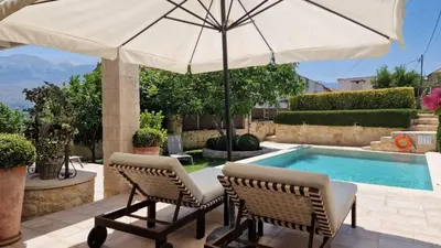 a patio with two chairs and an umbrella next to a swimming pool at Artemis Apollonas Villa I Luxury Escape with Pool in Káïna