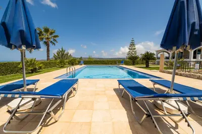 a swimming pool with two blue chairs and umbrellas at Villa Astrea in Sinoikismós Mamounianá