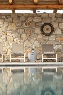 a stone wall with two chairs and a swimming pool at Villa Alargo Heated Pool in Katokhórion