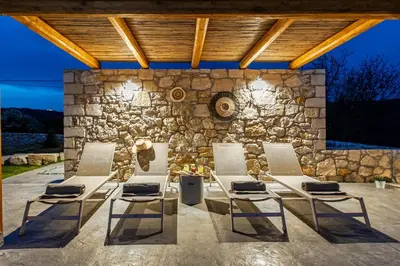a patio with four chairs and a stone wall at Villa Alargo Heated Pool in Katokhórion