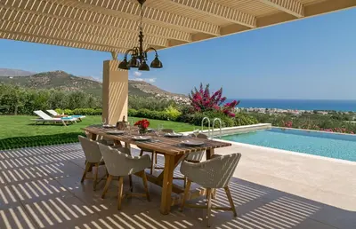 a wooden table and chairs on a patio with a pool at Villa Ianira in Kolymvari