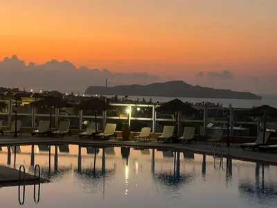 a swimming pool with chairs and umbrellas at sunset at Nea Kydonia suites and studios in Daratso