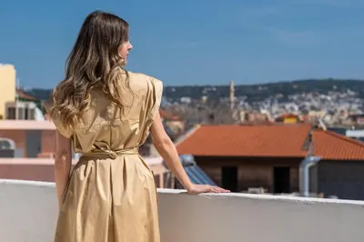 a woman in a gold dress looking out over a city at Mimosa Veneziano - Sauna - Old Town Chania in Chania Town