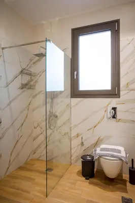 a bathroom with a glass shower with a toilet and a window at Polixenys home in Daratso