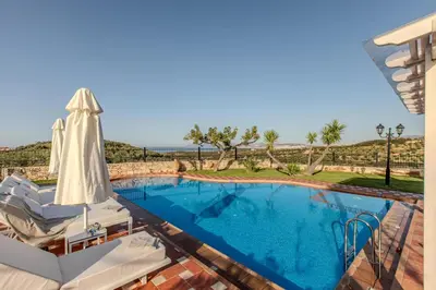 a swimming pool with an umbrella and chairs next to a swimming pool at Villa Trouli by Vintage Travel in Metókhi