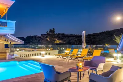 a patio with chairs and a swimming pool at night at Lucia's Home in Stalos