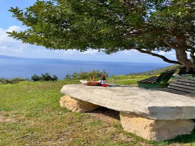 a person sitting on a stone bench under a tree at Seaview Studio in beautiful setting, west from Chania in Ravdhoúkha