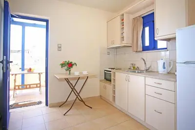 a kitchen with white cabinets and a table with flowers at Sfakia On the Beach in Khóra Sfakíon