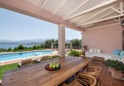 a patio with a wooden table and chairs and a swimming pool at Marathi Hilltop Oasis Sea View Villa in Marathi