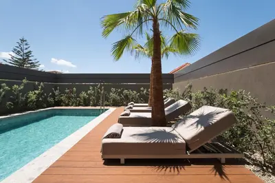 a row of lounge chairs next to a swimming pool with a palm tree at Memoire Guest House I Private Heated Pool I 200m beach in Chania Town