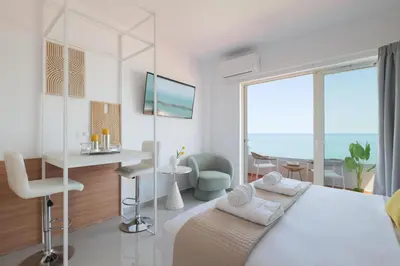 a white bedroom with a bed and a desk and a window at Stavros Beachfront Suites in Agia Marina Nea Kydonias