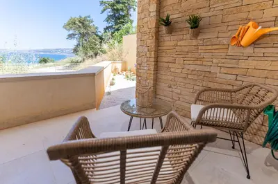 a patio with chairs and a table and a brick wall at Kymvari - Stunning sea view-elegant apt-infinity shared pool in Kalyves