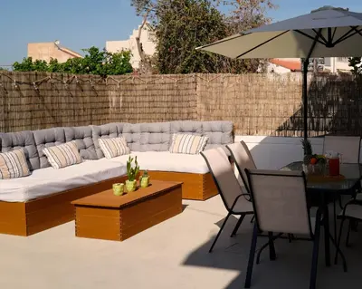 a patio with a couch and a table and an umbrella at IKARUS apartment with courtyard & pool in Chania in Stérnai