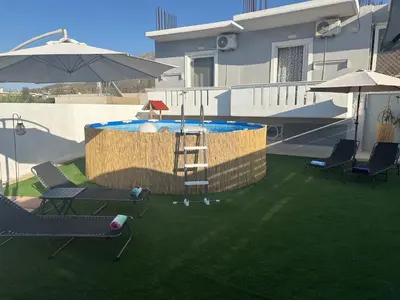 a pool with chairs and an umbrella on a yard at Vila Alexandros in Souda