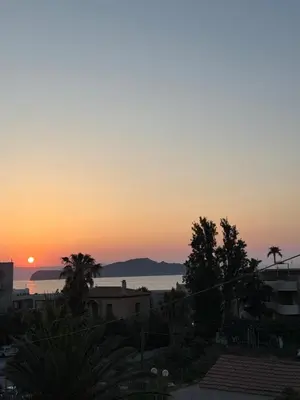 a sunset over the ocean with palm trees and buildings at Kalamaki Del Mar in Chania Town