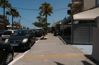 a street with parked cars and a sidewalk with palm trees at Kalamaki Del Mar in Chania Town