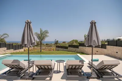 a group of chairs and umbrellas next to a pool at Kymélia Luxury Residences With Sea View in Galatás