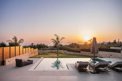 a patio with chairs and an umbrella and the sunset at Kymélia Luxury Residences With Sea View in Galatás
