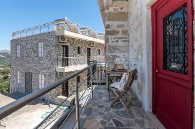 a balcony with a red door and a chair at The Mulberry Stonehouse Mountain - Sea View in Kalleryianá