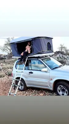 a person sitting on top of a car with a tent on top at Rooftop Jeep Escape Sleep Under the Stars in Chania Town