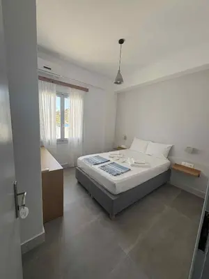 a white bedroom with a bed and a window at Nikolas Rooms in Loutro
