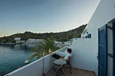 a person sitting on a balcony looking at the water at Nikolas Rooms in Loutro