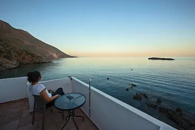 a woman sitting on a balcony looking at the water at Nikolas Rooms in Loutro