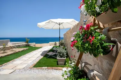 a garden with flowers and an umbrella and the ocean at The Seaside Nest in Chania Town