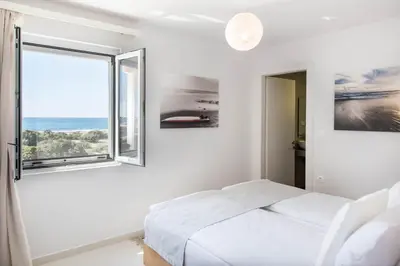 a white bedroom with a bed and a window at Falasarna Seafront House I 50m to the Beach in Kavoúsion