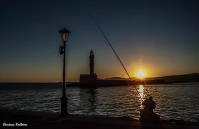 a man sitting next to the water with a lighthouse at Castle Inn in Chania Town