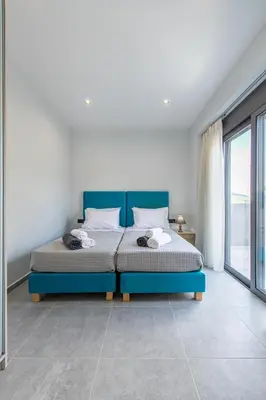 a bedroom with a blue bed and a large window at Neaira Apartments in Vatólakkos