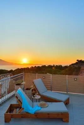 a balcony with a couch and a table and the sunset at Villa Ravdoucha in Ravdhoúkha