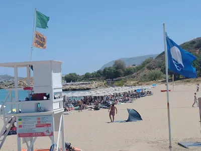 a crowd of people on a beach with a blue flag at Hillside Escape by the Sea in Daratso