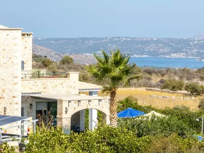 a palm tree in front of a building with a view of the ocean at Villa Enid in Sinoikismós Mamounianá