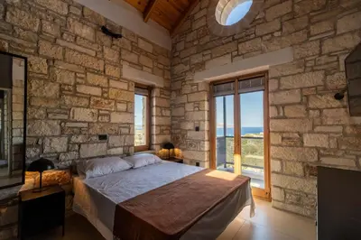 a stone walled bedroom with a bed and a large window at Villa Seiri by PosarelliVillas in Gavalochori
