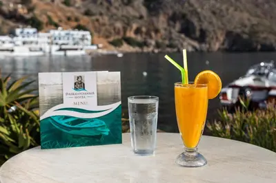 a glass of orange juice and a book on a table at Daskalogiannis Hotel in Loutro