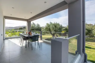 a patio with a table and chairs and a large window at Adriana Horizon Villa, Pool & Hillside View in Galatás